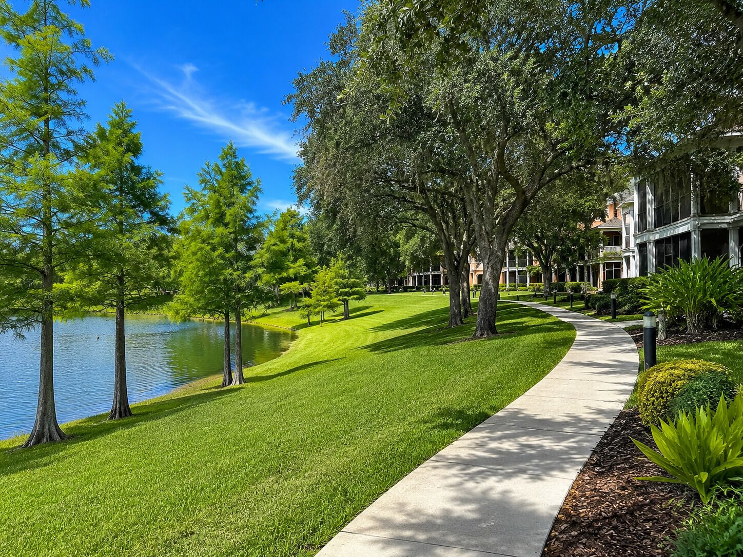 A well-maintained park with a walking path, a body of water, and a building with a classic architectural style.