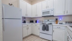 A kitchen with white cabinets, a refrigerator, a microwave, an oven, and a coffee maker.