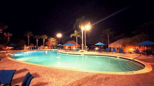 A nighttime swimming pool area with lounge chairs and umbrellas.