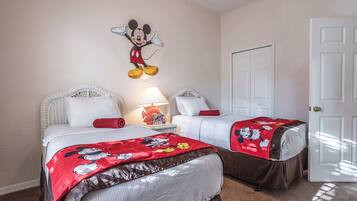 A hotel room with two beds, each with Mickey Mouse-themed bedding. There is a wall-mounted Mickey Mouse decoration and a lamp on a nightstand.