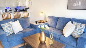 A living room with a blue sofa set, a wooden coffee table, and a vase with flowers.