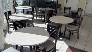 Ett hotellrum med en matplats som har runda bord och trästolar, ett stort fönster med persienner och en dörr med en skylt.