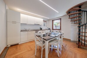 A modern kitchen with white cabinets, a dining table set for four, and a spiral staircase. - ApartmentsArena - Capitolium Verona 6 (Verona)
