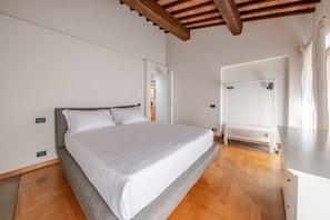 Ein Schlafzimmer mit Bett, Holzboden, weißer Wand und Decke mit freiliegenden Balken.