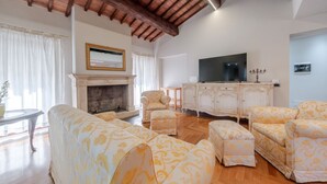 A living room with a fireplace, sofa set, television, and a ceiling with exposed beams. - ApartmentsArena - Capitolium Verona 6 (Verona)