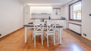 A modern kitchen with white cabinets, a dining table with chairs, a window with a view, and a built-in microwave. - ApartmentsArena - Capitolium Verona 6 (Verona)