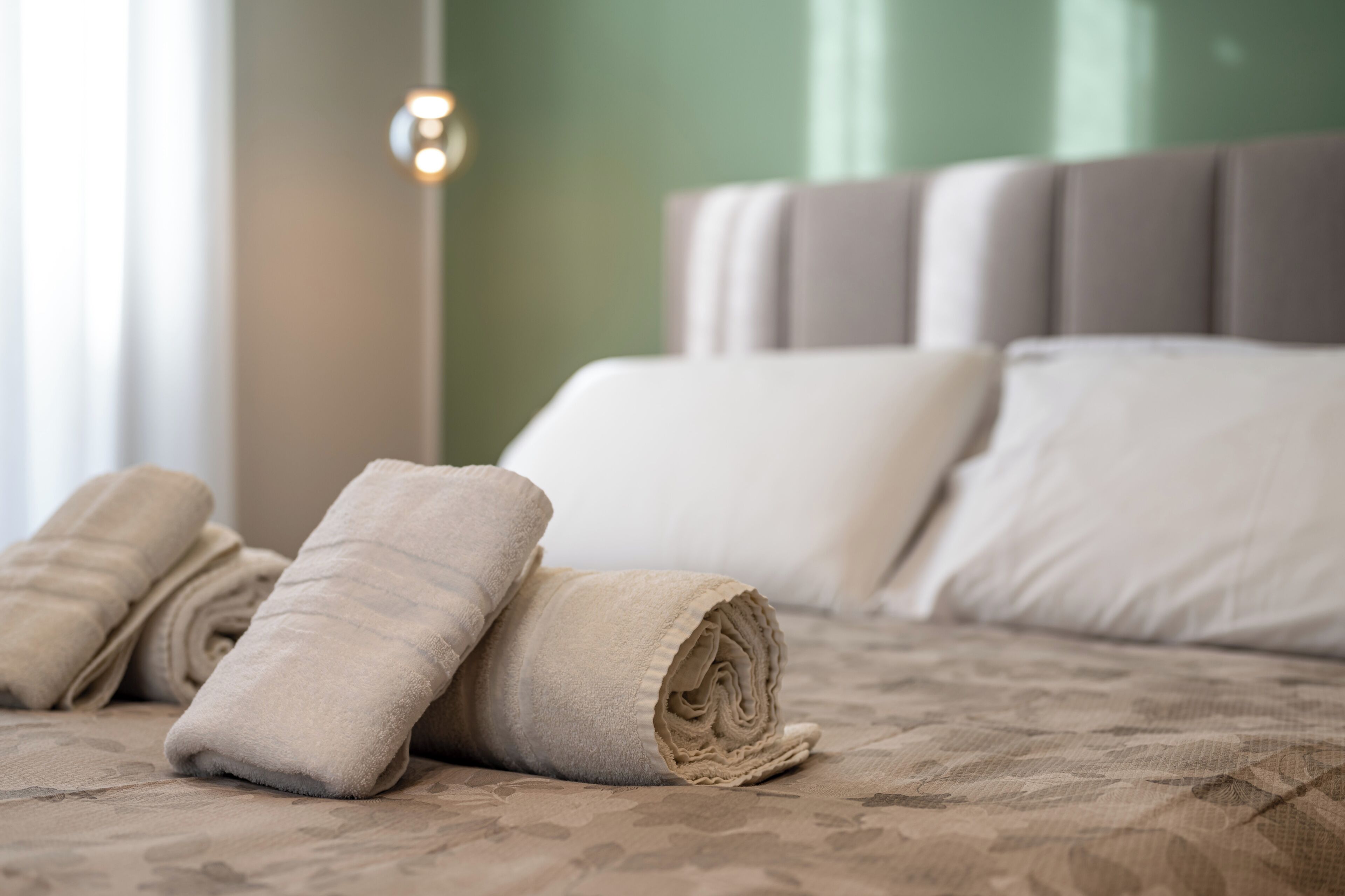 Een opgemaakt bed met opgerolde handdoeken en een hoofdeinde.