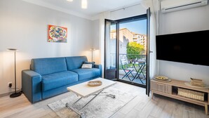 A modern living room with a sofa, a coffee table, a flat-screen TV, and a balcony with outdoor furniture. - Doux Zéphir – Marine Serenity and Tranquility by the Sea (Fréjus)