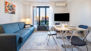 A modern living room with a blue sofa, a dining table with chairs, a flat-screen TV, and a large window with curtains. - Doux Zéphir – Marine Serenity and Tranquility by the Sea (Fréjus)