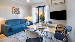 A modern living room with a blue sofa, dining table set, and a TV mounted on the wall. - Doux Zéphir – Marine Serenity and Tranquility by the Sea (Fréjus)