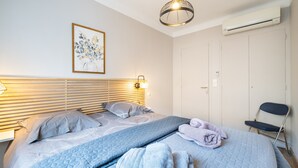 A bedroom with a bed, pillows, a blanket, a towel, a hanging light fixture, a wall-mounted air conditioner, and a chair. - Doux Zéphir – Marine Serenity and Tranquility by the Sea (Fréjus)