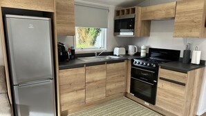 Eine kleine Küche mit Holzschränken, einem Edelstahlkühlschrank, einer Mikrowelle, einem Herd und einem Spülbecken.