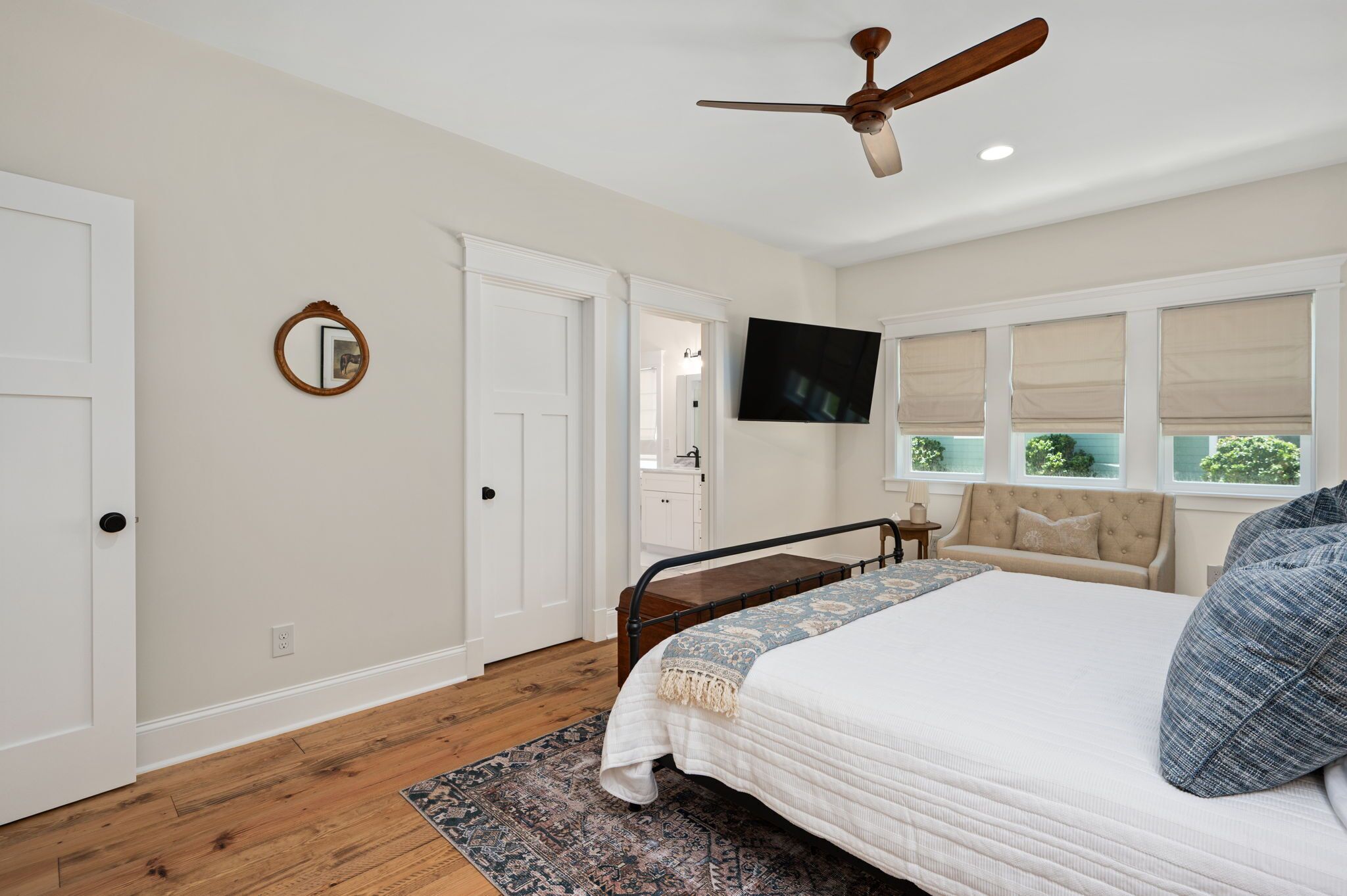 A bedroom with a bed, a ceiling fan, a TV, and a window with blinds.