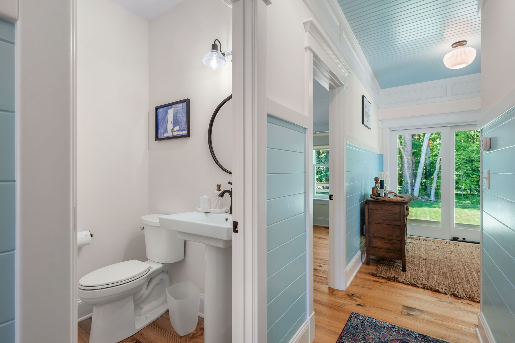 A bathroom with a toilet, sink, and a mirror. There is a window with a view of trees.