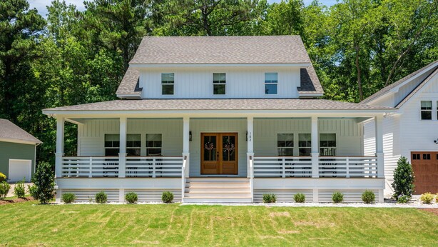 A two-story house with a front porch, a wooden door, and a small front yard. - Discover this stunning award-winning luxury 4br & 3.5 bath home in the OBX (Powells Point)
