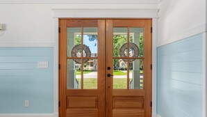 A wooden double door with glass panels and a view of a residential street. - Discover this stunning award-winning luxury 4br & 3.5 bath home in the OBX (Powells Point)