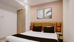 Ein Hotelzimmer mit einem Bettgestell aus Holz, einer Kopfteil, einem Nachttisch mit Telefon und zwei an der Wand befestigten Kunstwerken.