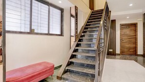 Eine Treppe mit Holzhandlauf und schwarzen Stufen, eine rote Bank, ein großes Fenster mit Jalousien und eine Tür mit der Nummer 101.
