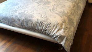 Ein Bett mit einem blumigen Bettüberwurf, zwei Kissen, einer Nachttischlampe und einem Nachttisch.