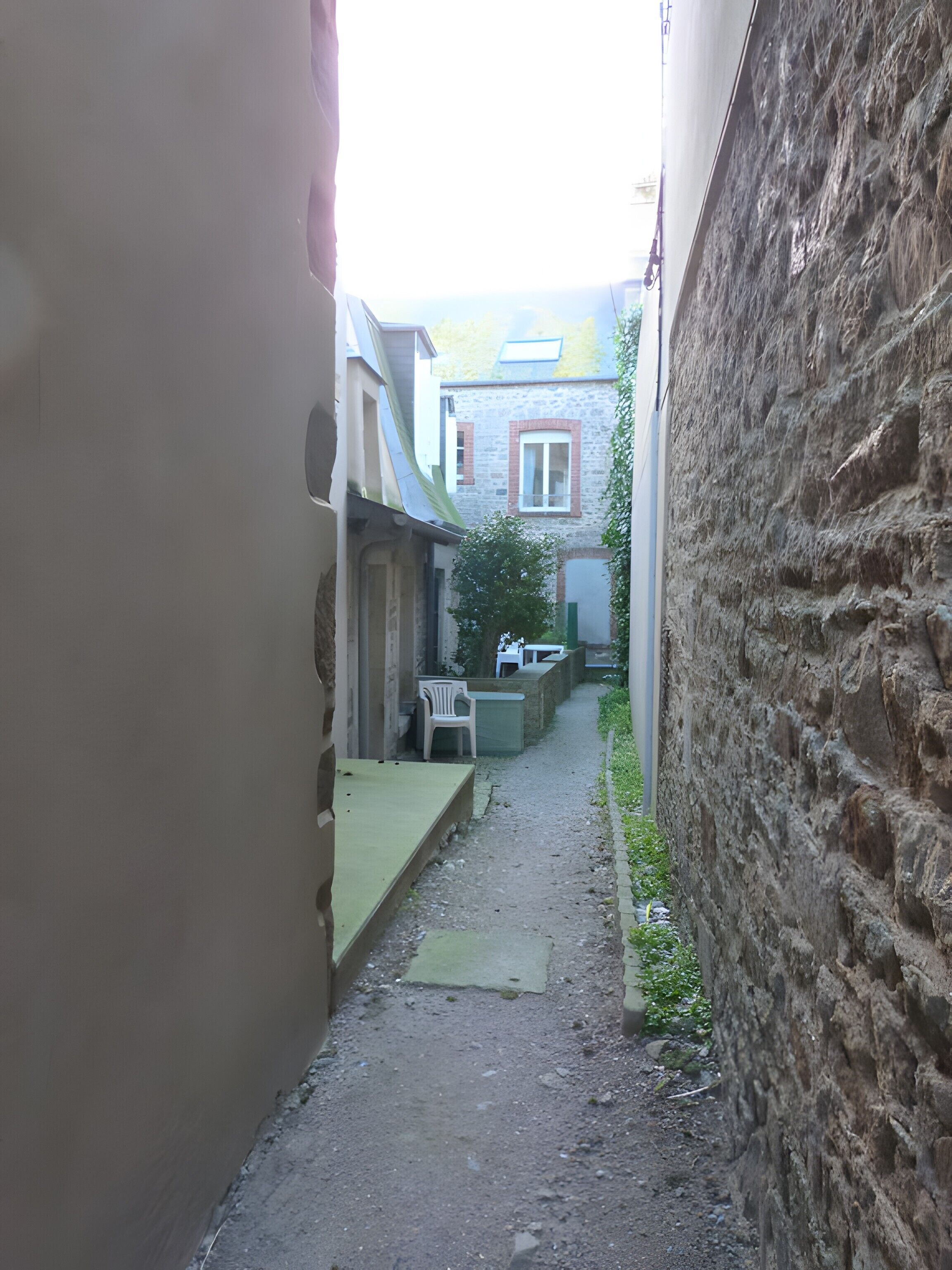 Une ruelle étroite avec un chemin de gravier, une chaise en plastique blanche et une table.