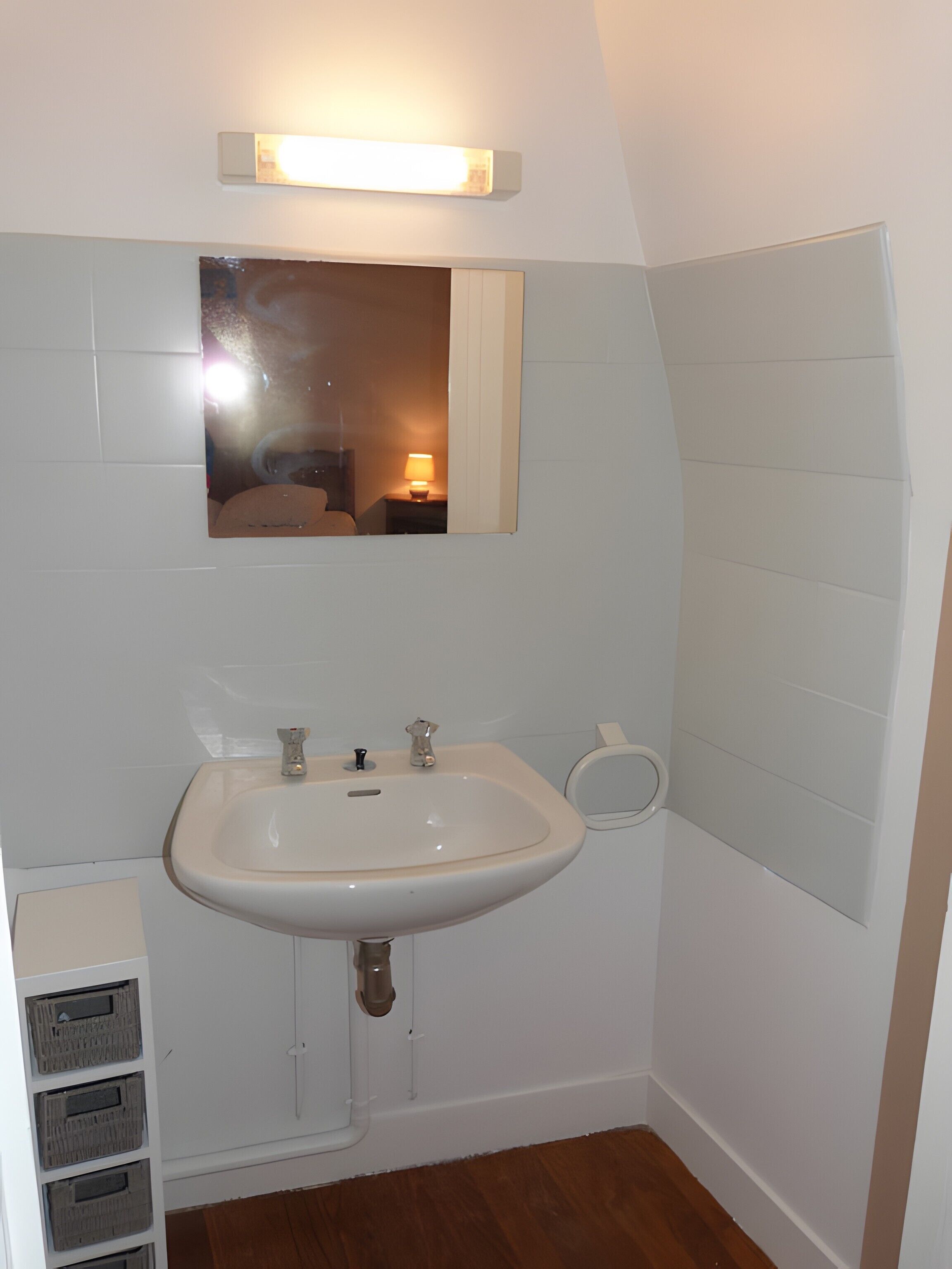 Une salle de bain équipée d’un lavabo, d’un miroir et d’un luminaire fixé au mur.