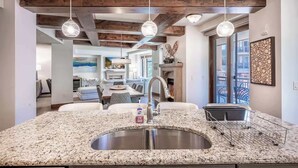 A modern kitchen with granite countertops, a stainless steel sink, pendant lighting, and a view to a dining area.