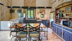 Une cuisine dotée d’un îlot central, d’une table à manger et de chaises, avec des murs en pierre et des meubles de rangement en bois.