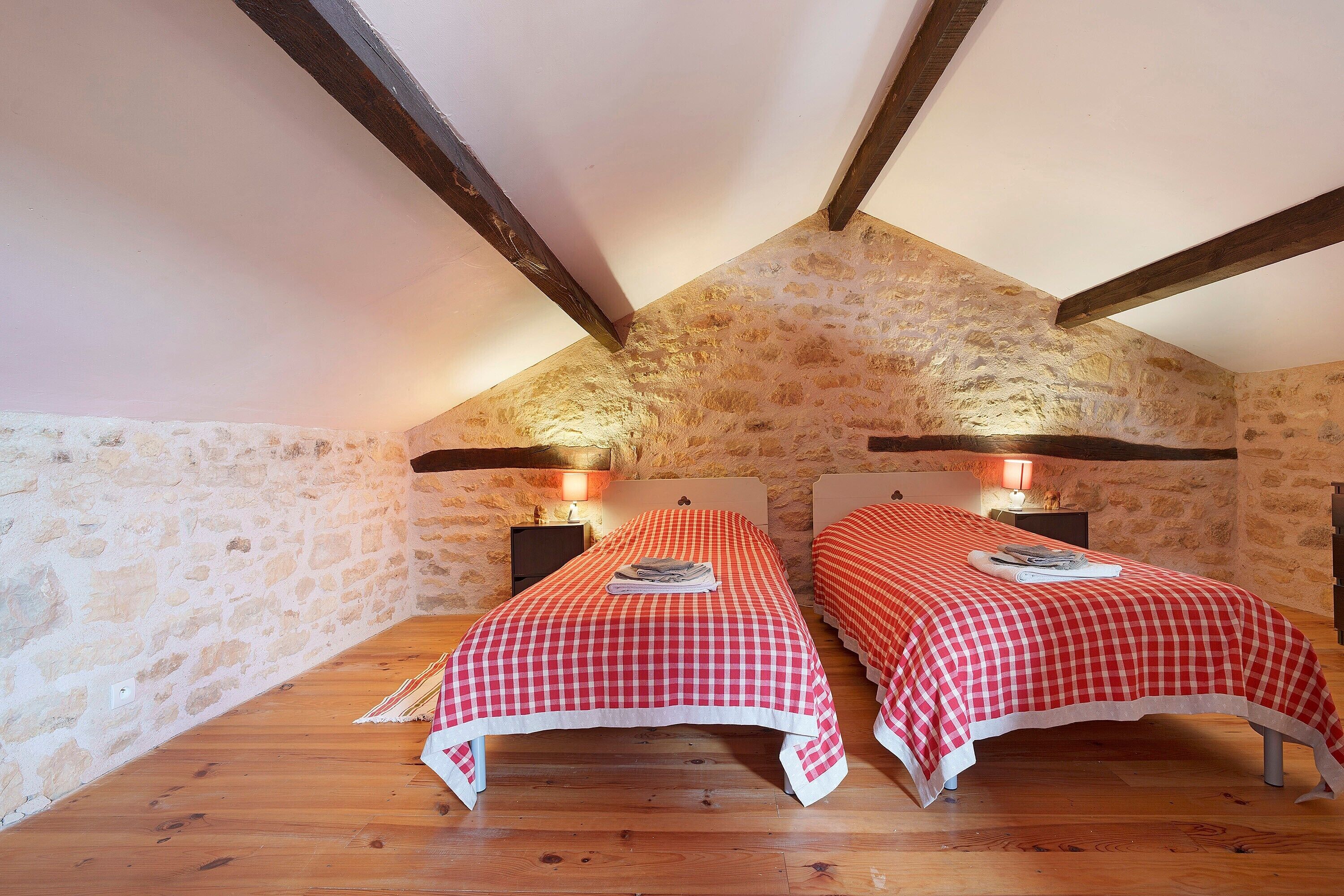 A bedroom with two beds, stone walls, wooden beams, and a sloped ceiling.