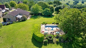 Une grande maison avec une piscine, entourée d’une pelouse bien entretenue et d’arbres.