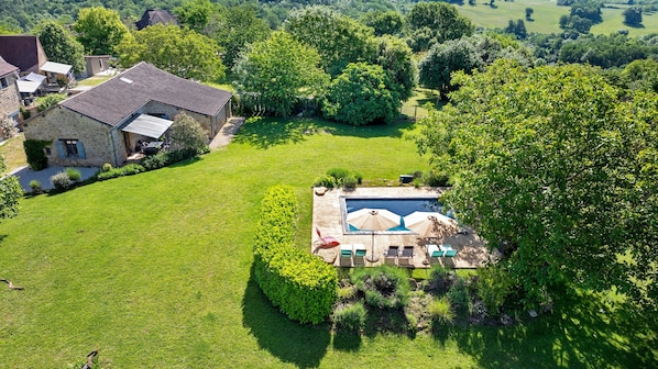 Une grande maison avec une piscine, entourée d’une pelouse bien entretenue et d’arbres.
