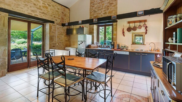 Une cuisine avec un coin repas, des murs en pierre et une vue sur l’extérieur, accessible par une porte-fenêtre coulissante.