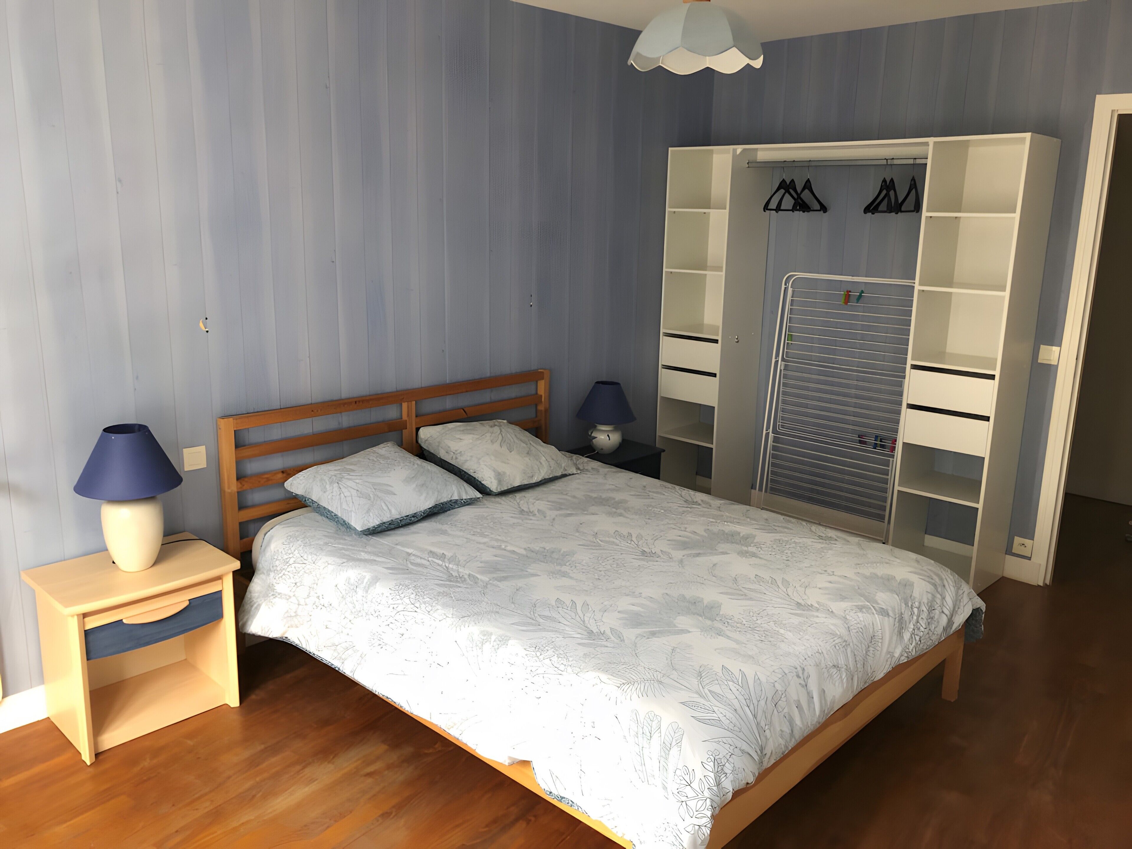 Une chambre à coucher avec un lit en bois, une table de chevet, une lampe, une armoire et un porte-vêtements.