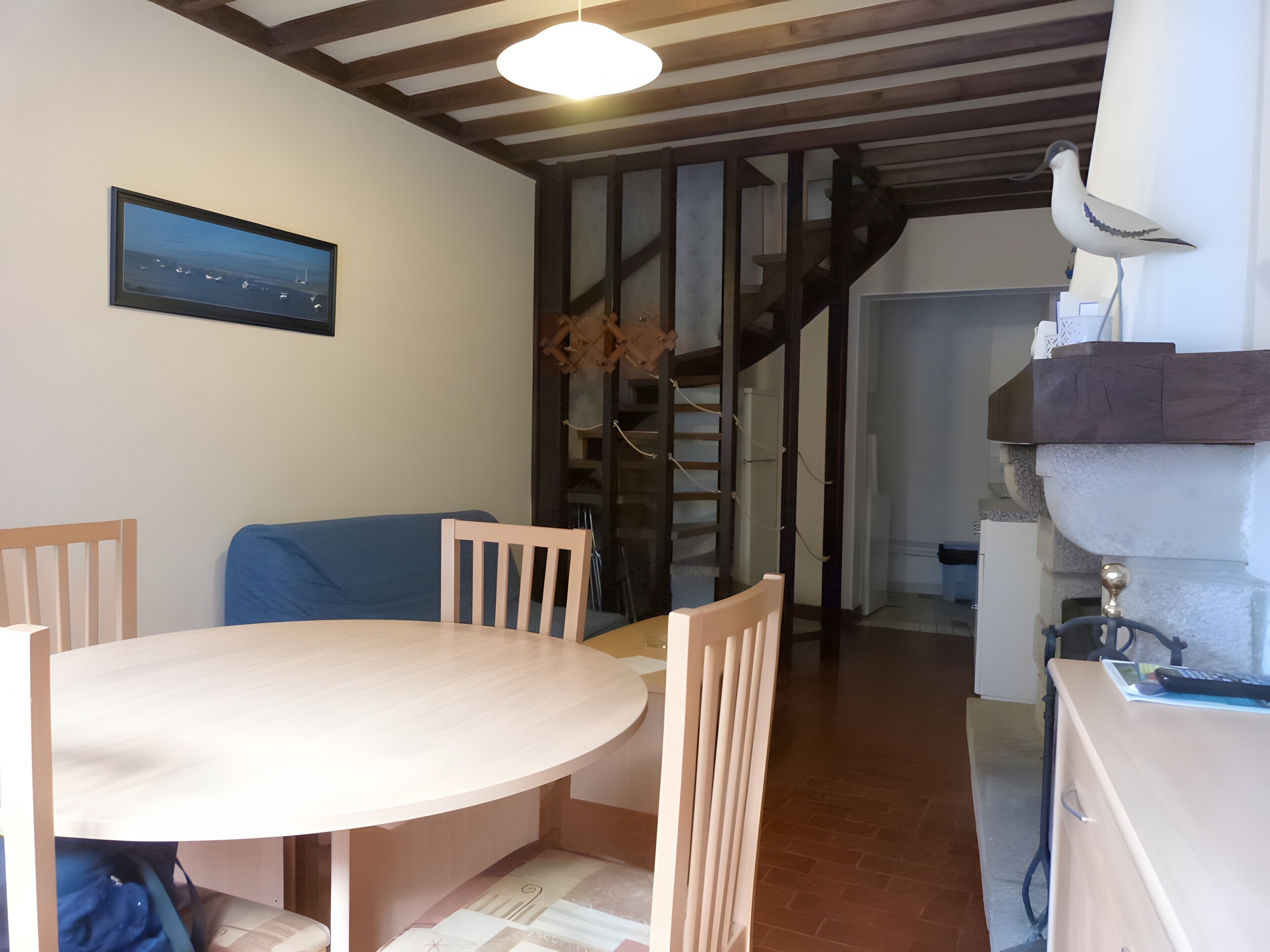 Et spiseområde med et rundt bord, stole, en blå sofa, en trappe og en vægmonteret lampe.