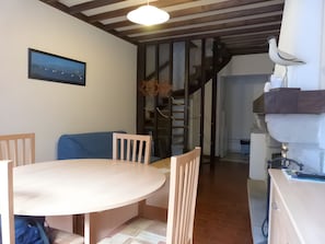 Un espace repas comprenant une table ronde, des chaises, un canapé bleu, un escalier et un luminaire fixé au mur.