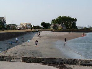 Une plage avec un mur de pierres, des maisons et un ciel dégagé.
