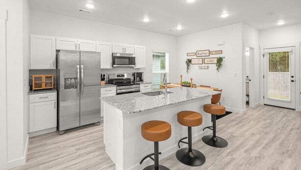 A modern kitchen with white cabinets, stainless steel appliances, a granite countertop, and a bar area with stools. - Modern 3BR Centerton Near Walmart HQ & Bentonville (Centerton)