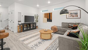 A modern living room with a flat-screen TV, a grey sofa, a coffee table, and a large window. - Modern 3BR Centerton Near Walmart HQ & Bentonville (Centerton)