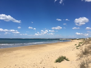 Ein weiter Sandstrand mit sanften Wellen, blauem Himmel und vereinzelten Wolken.