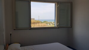 Ein Schlafzimmer mit einem Einzelbett, einem Fenster mit Milchglas und Blick auf das Meer und die Vegetation.