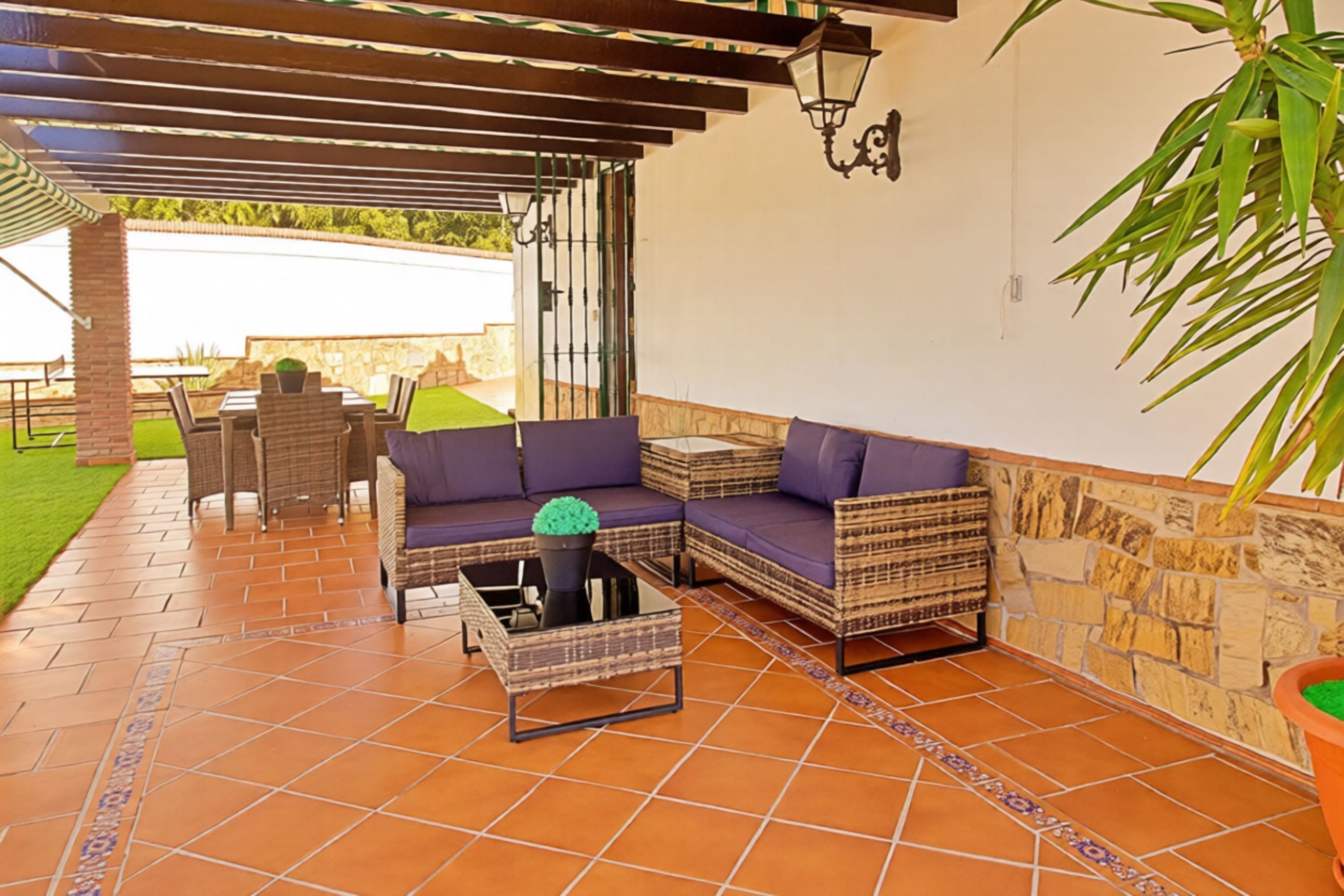 Un espacio de patio cubierto con mobiliario de mimbre, piso de baldosas y pared de piedra.