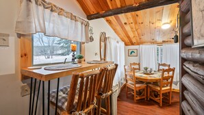 Une table à manger en bois avec des chaises, une fenêtre avec des rideaux et un plafond en bois.