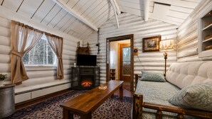 L’intérieur d’une cabane en rondins, avec une cheminée, un téléviseur, un canapé et un tapis à motifs.