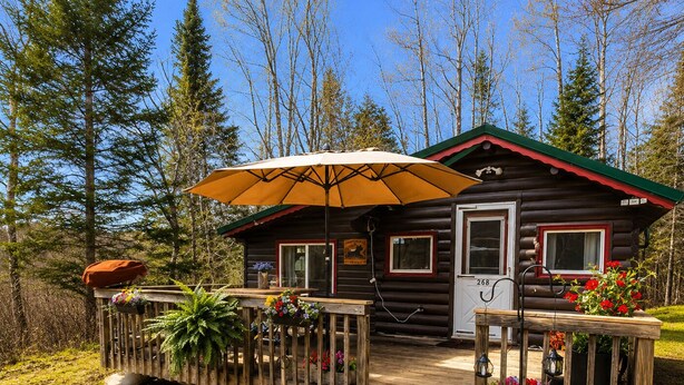 Une cabane en rondins avec une terrasse en bois, un porche et un grand parasol.