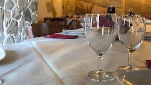 A restaurant with stone walls, wooden beams, and a table set with wine glasses and plates. - Locanda Il Tempo (Cleto)