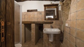 A bathroom with a stone-tiled floor, a wooden bench, a sink, and a mirror. - Locanda Il Tempo (Cleto)