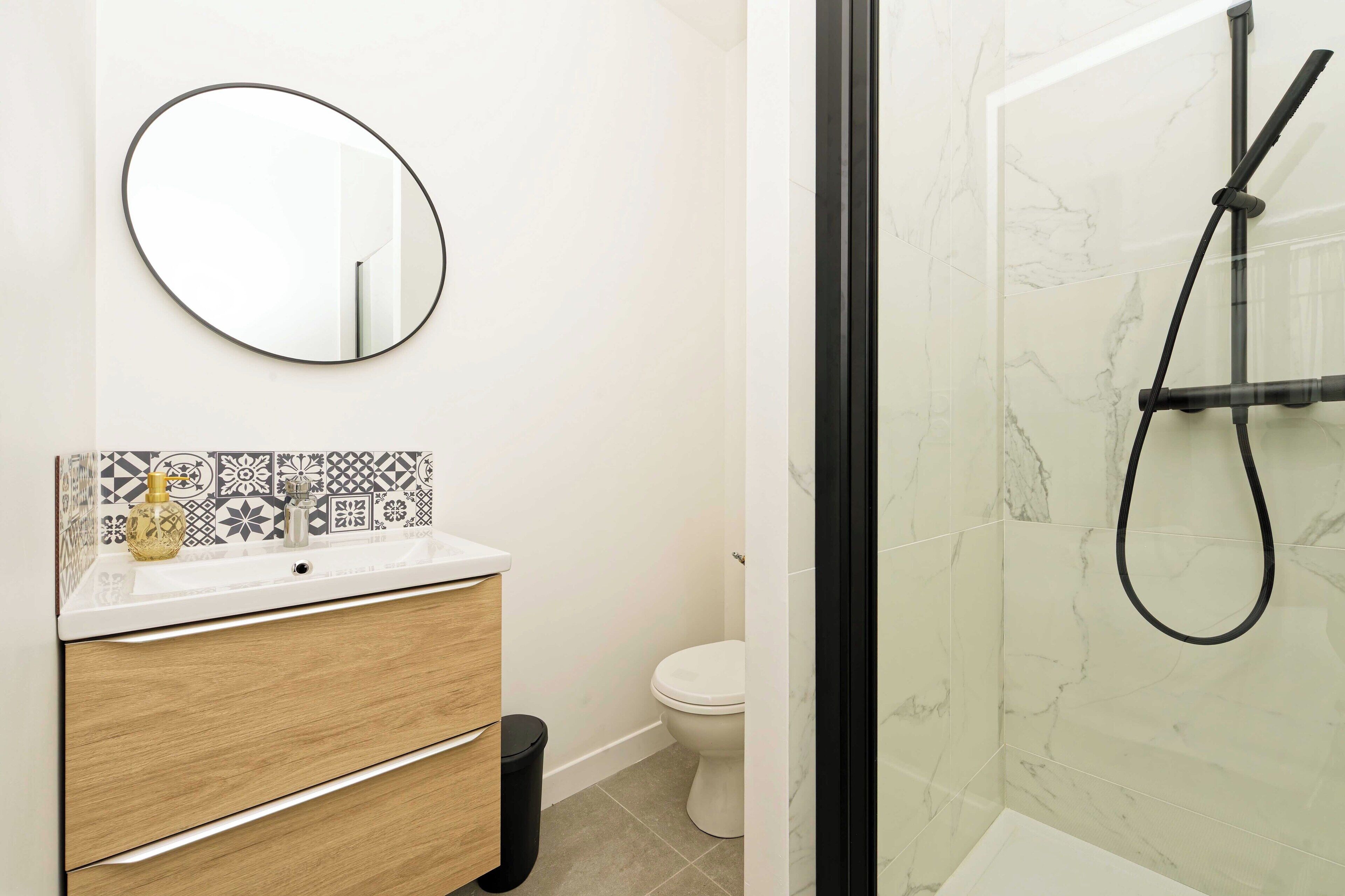 Une salle de bain avec un lavabo blanc, un miroir, des toilettes et un espace douche doté d’une porte en verre.