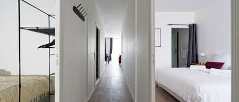 A hotel room with a bed, a desk, and a chair. There is a hallway leading to another room.