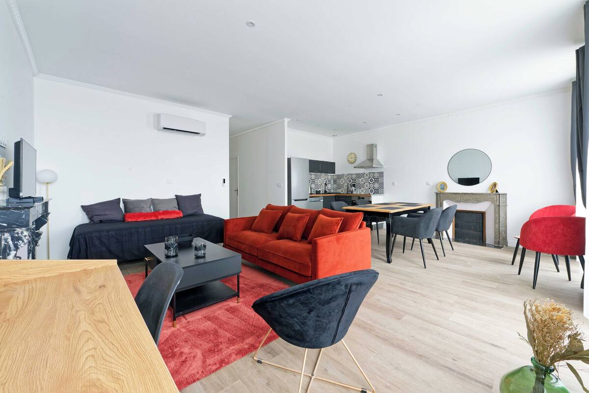 A modern living room with a red sofa, black armchair, and a dining area with a table and chairs.