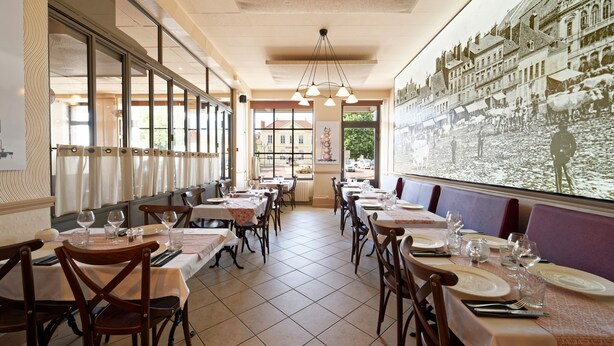 A restaurant with long tables, chairs, and a large window with a view of a street scene. - Villa Napoléon - Au coeur d'Autun (Autun)