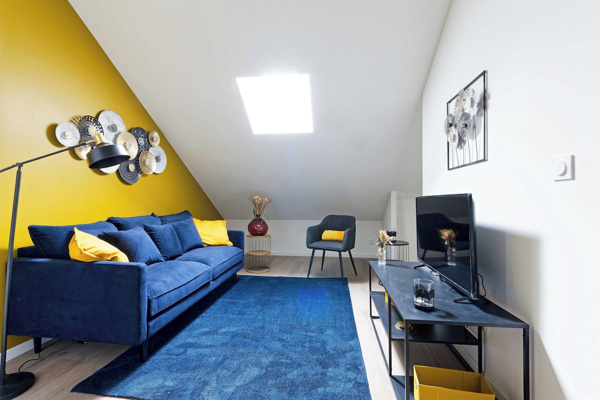 A modern living room with a blue sofa, a black desk, and a yellow accent wall.